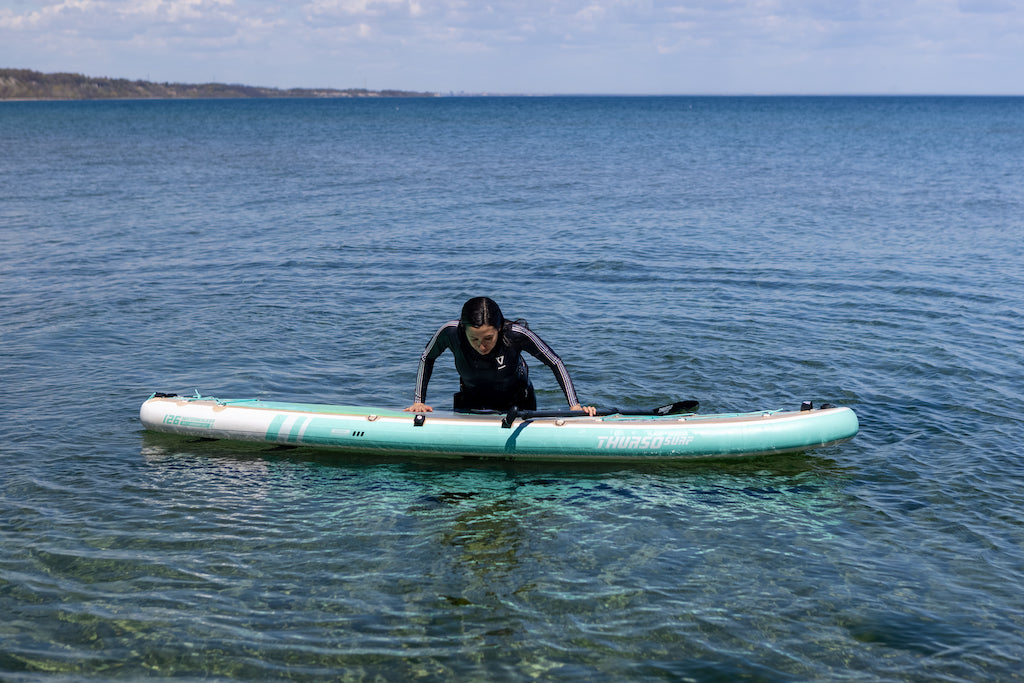Woman demonstrating how to get back on a paddleboard after falling in the water