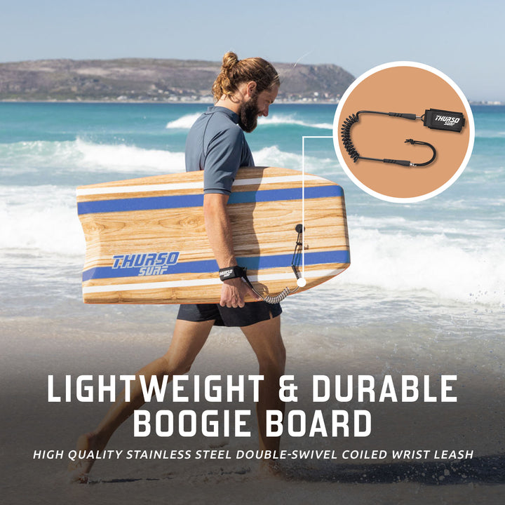 A man carrying an Azure blue wood-grain Thurso Surf boogie board on a beach, featuring a high-quality stainless steel coiled wrist leash
