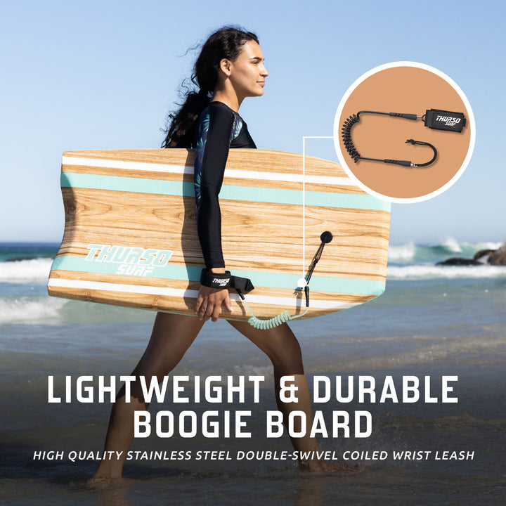 A woman walking on a beach carrying a turquoise wood-grain Thurso Surf Quill bodyboard under her arm, ready for surfing