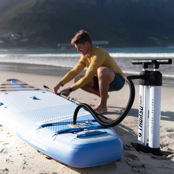 Person preparing a dusk paddleboard on a beach with a pump nearby