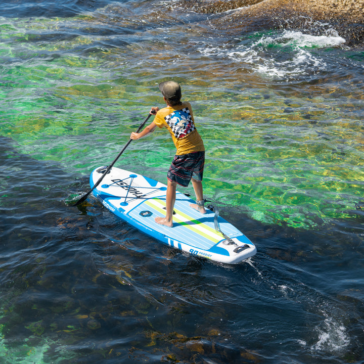 High-angle view of a child paddling an azure and white inflatable SUP board on vibrant coastal waters.