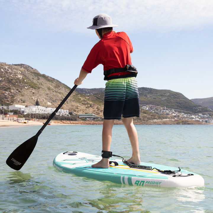 High-angle view of a young paddler on an Emerald green Thurso Surf Prodigy paddle board, gliding over clear turquoise water.