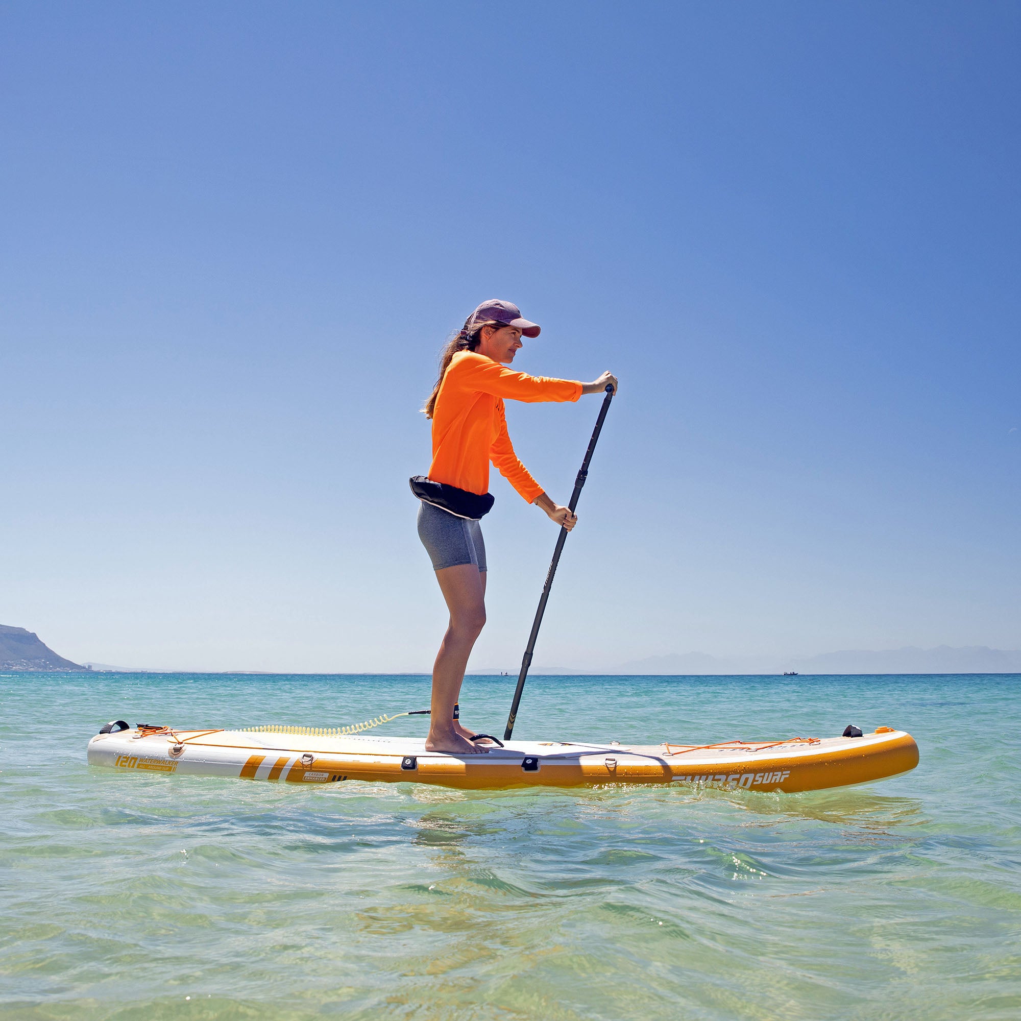 A woman stand-up paddleboarding on a Tangerine-colored waterwalker 120 paddleboard on calm water.