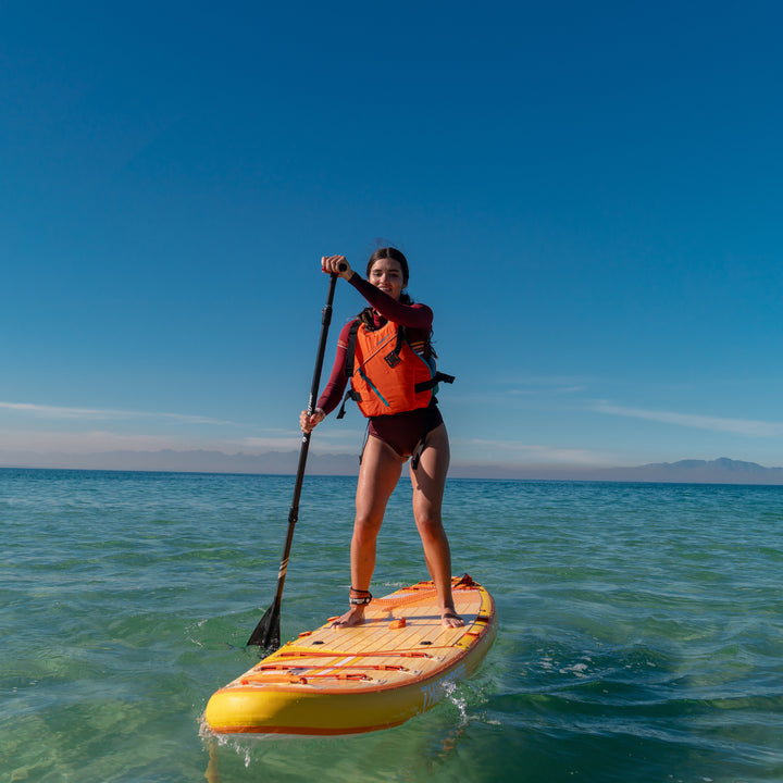 Person paddleboarding on a clear blue ocean with a life jacket on tangerine waterwalker 120