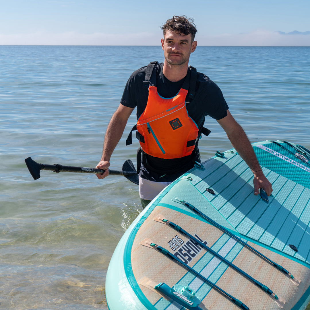 Man with a paddle and turquoise paddleboard in shallow water