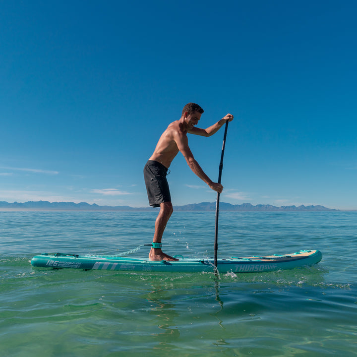 Man paddling a turquoise thurso surf waterwalker 126 on a clear day with mountains in the background